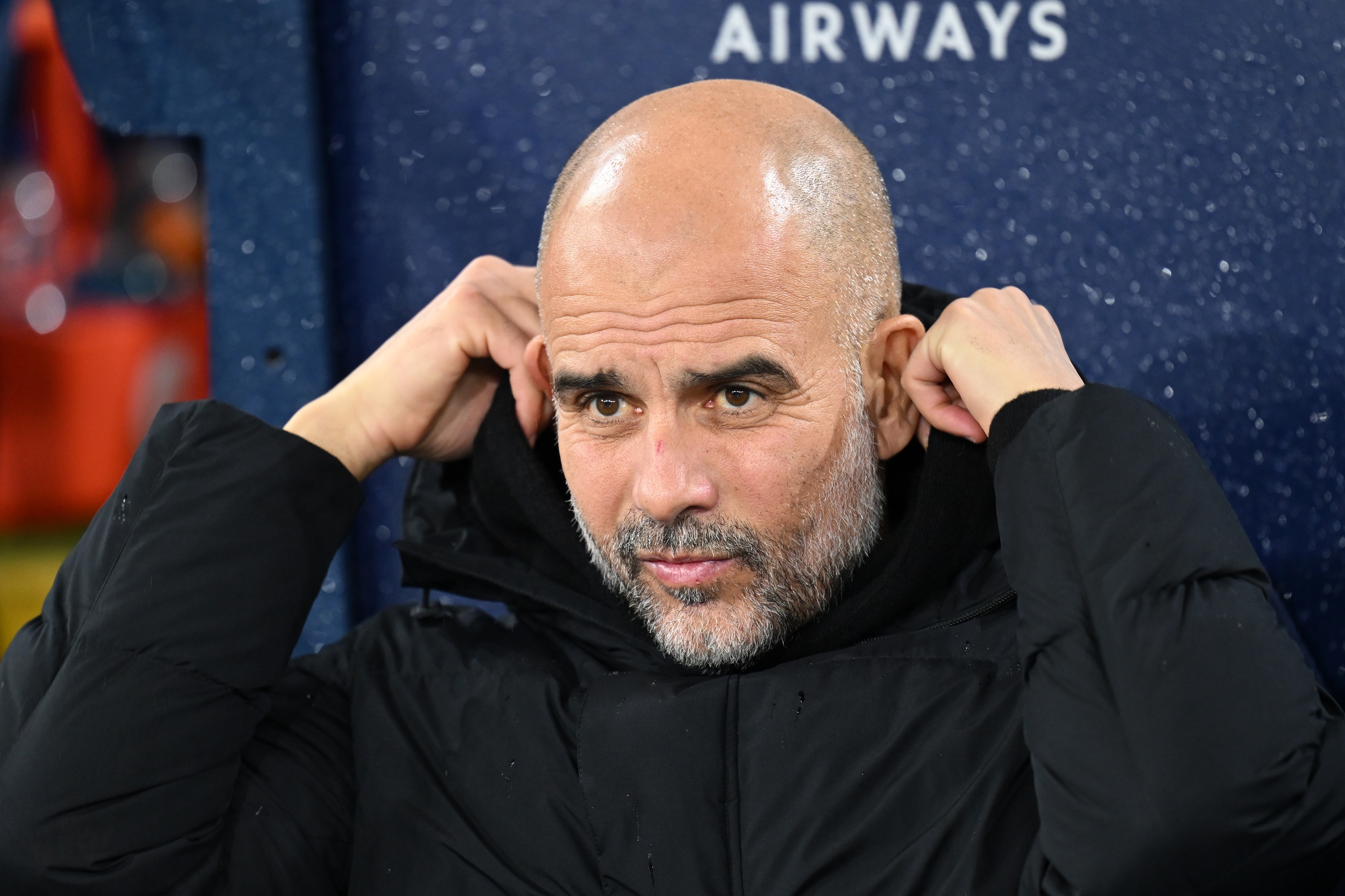 Pep Guardiola lifts up his hood to protect against rainfall.