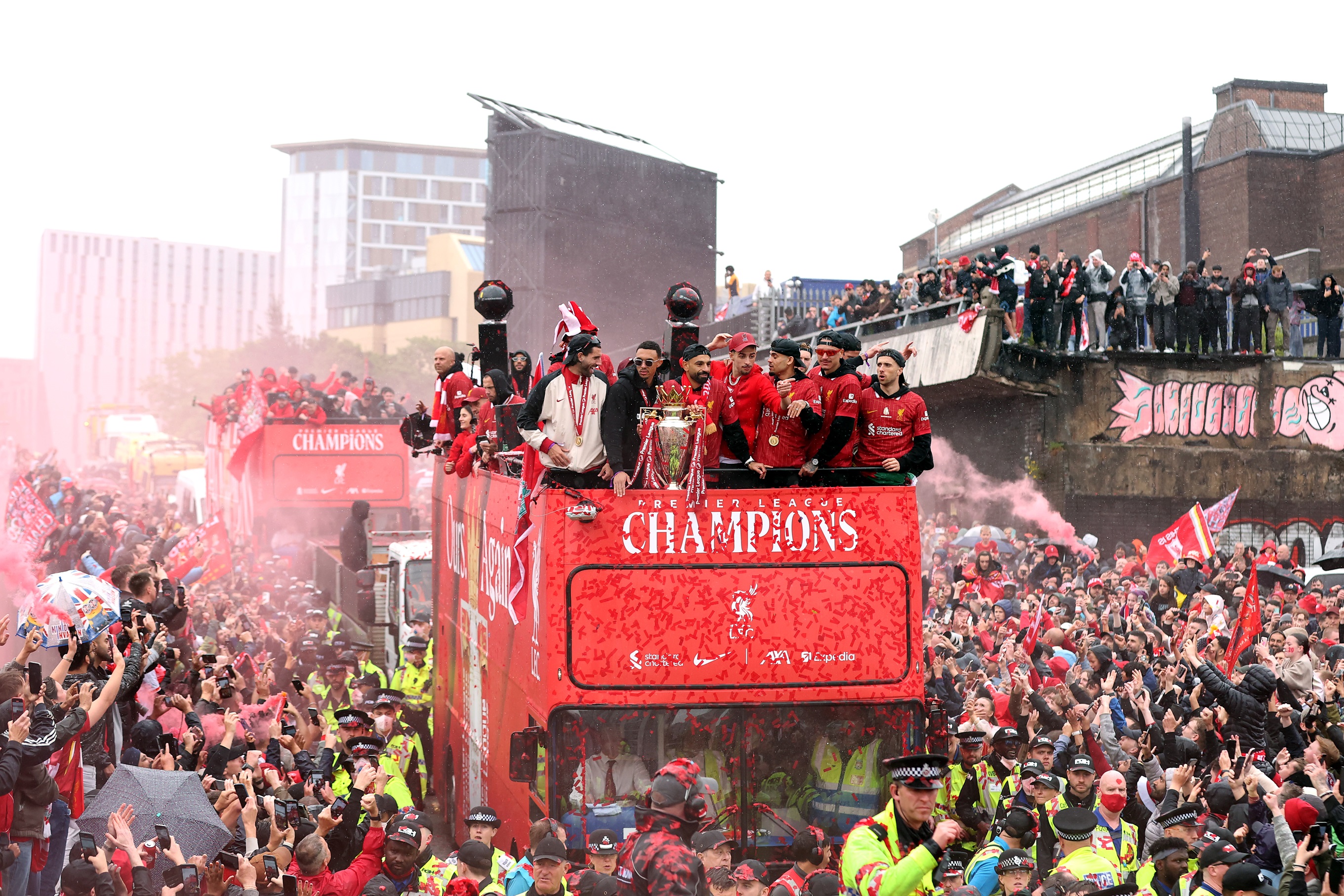 Liverpool players celebrate with Premier League trophy on open top bus.