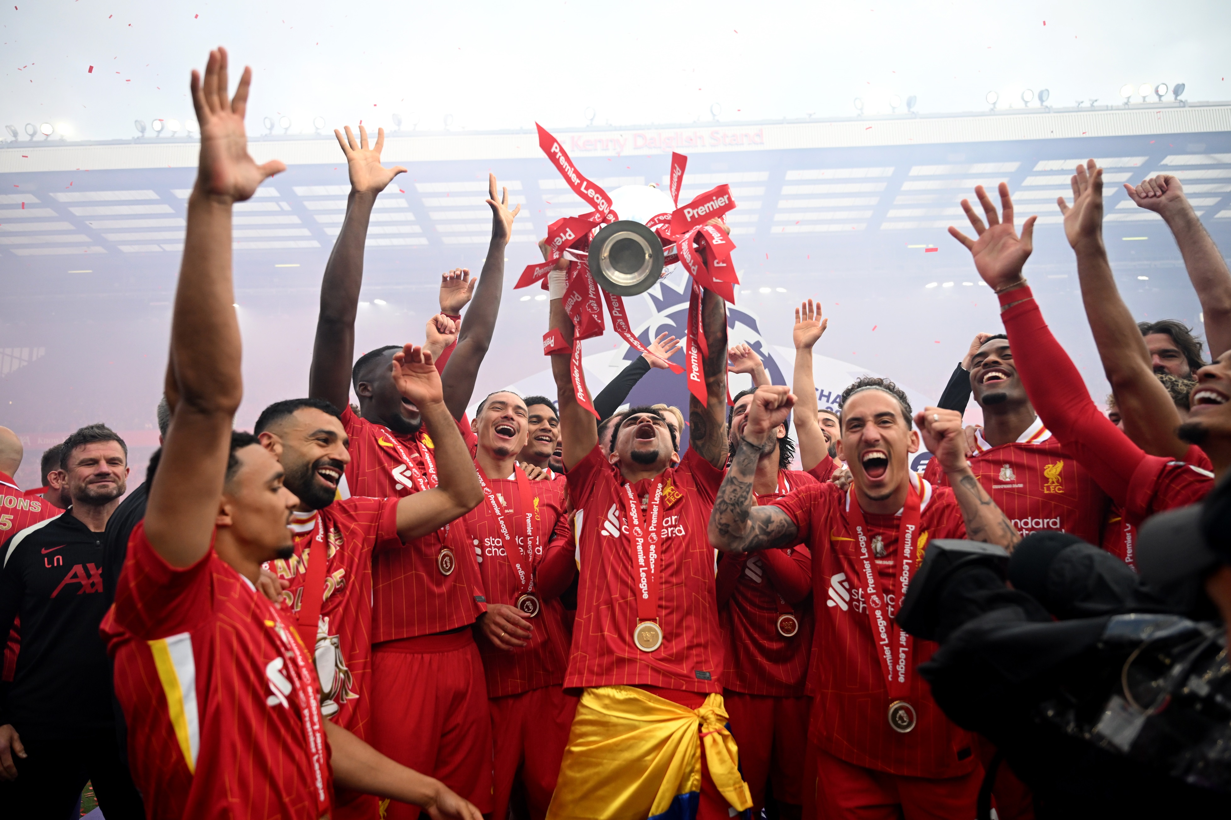 Luis Diaz lifts Premier League trophy in the air while surrounded by Liverpool players.