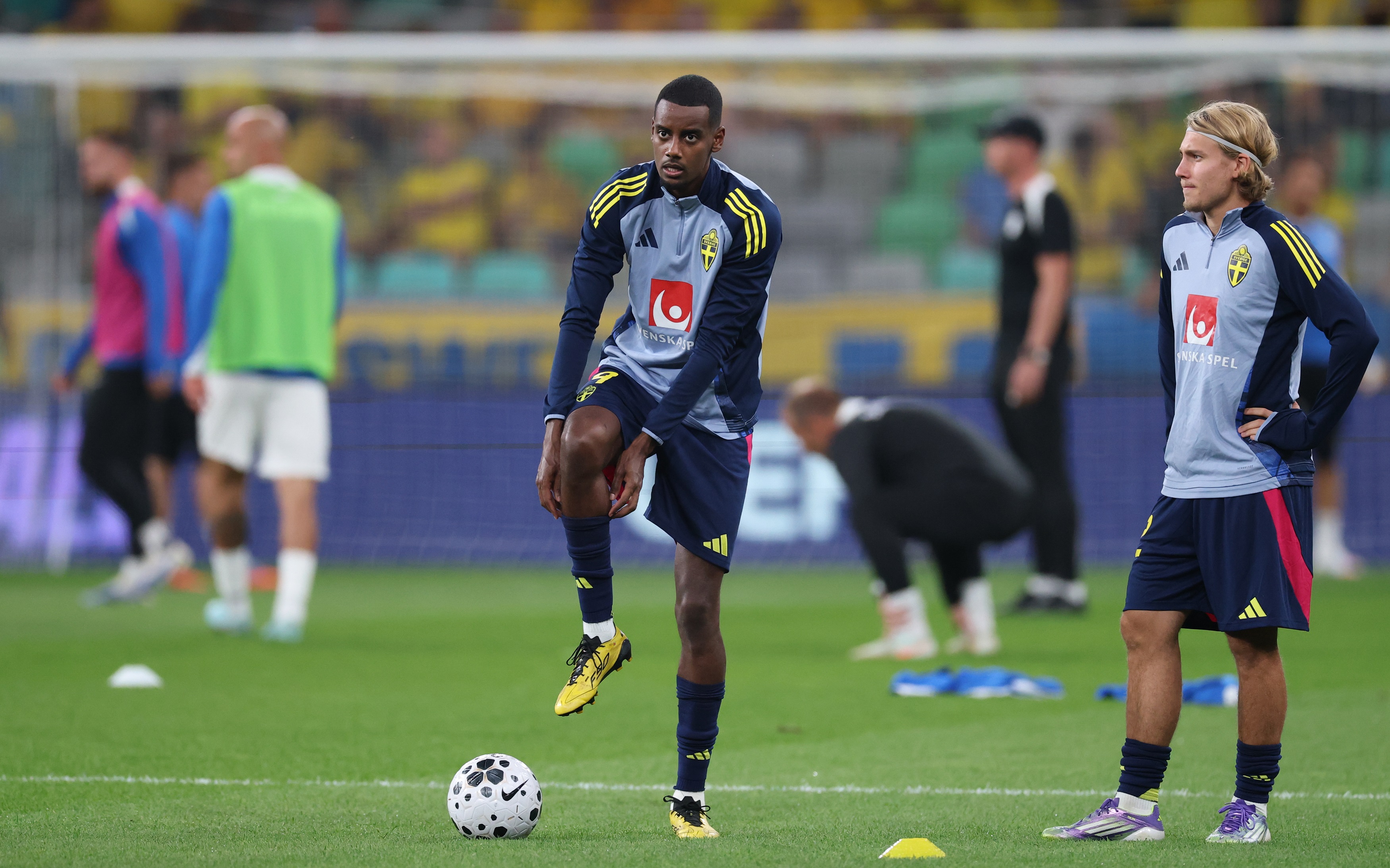 Alexander Isak pulls up his sock on his raised right leg.