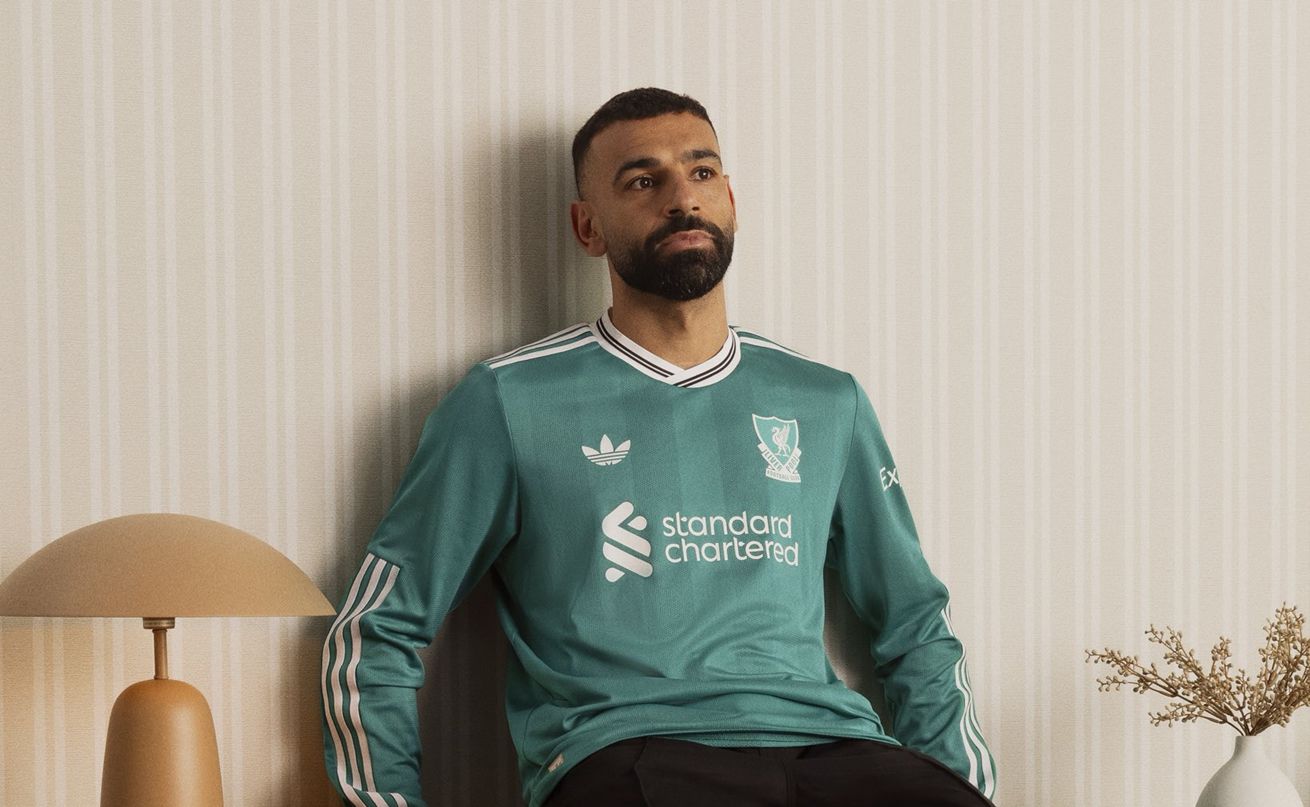 Mo Salah sits on a piece of furniture looking thoughtful.