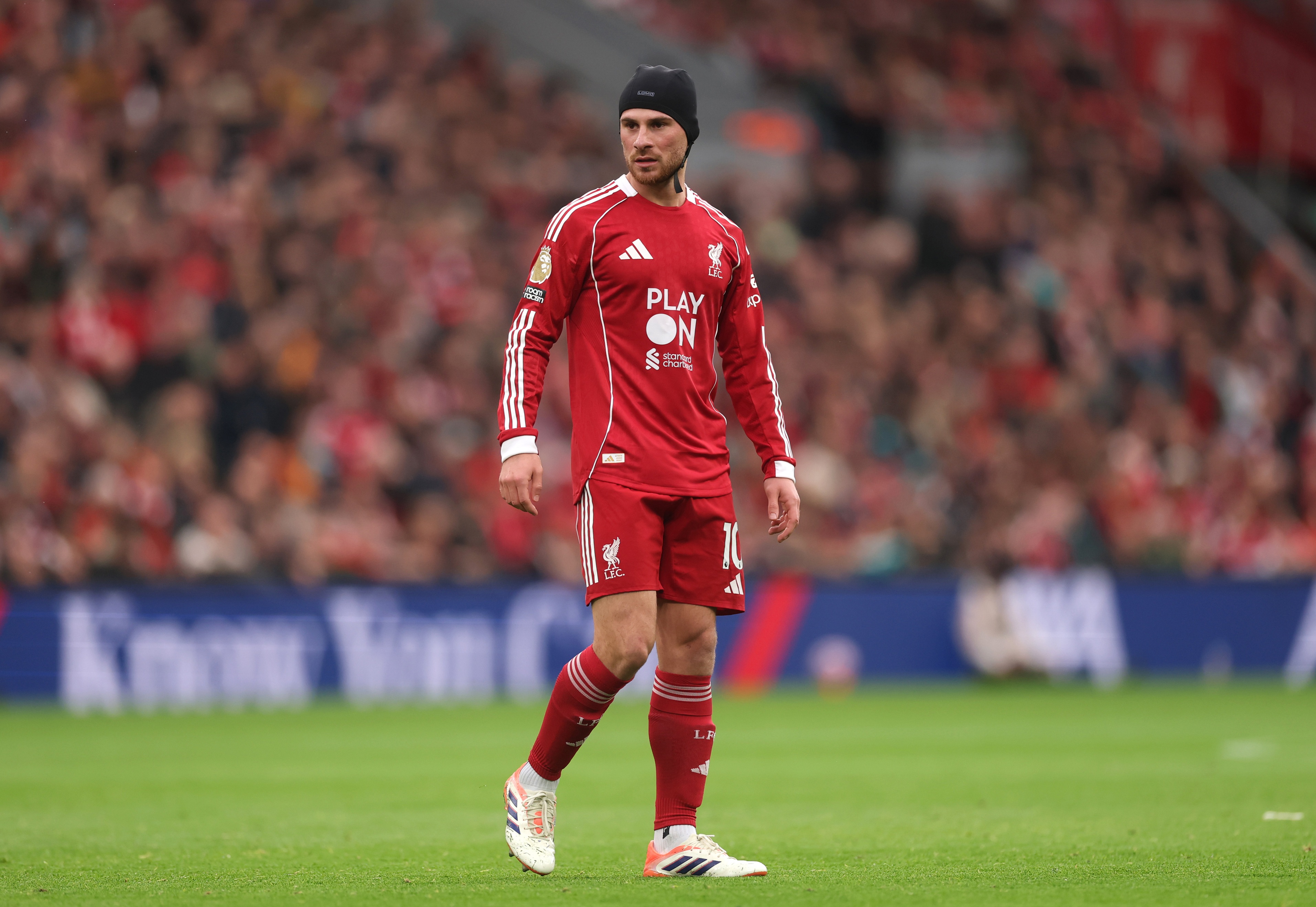 Alexis Mac Allister walks on the pitch with a head cap.
