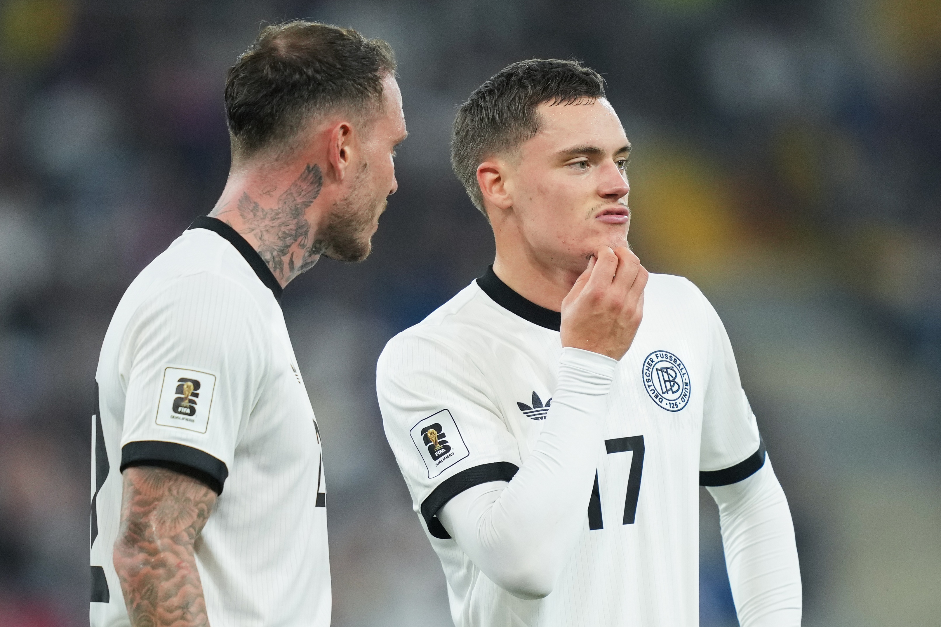 Florian Wirtz scratches his chin whilst talking with David Raum.