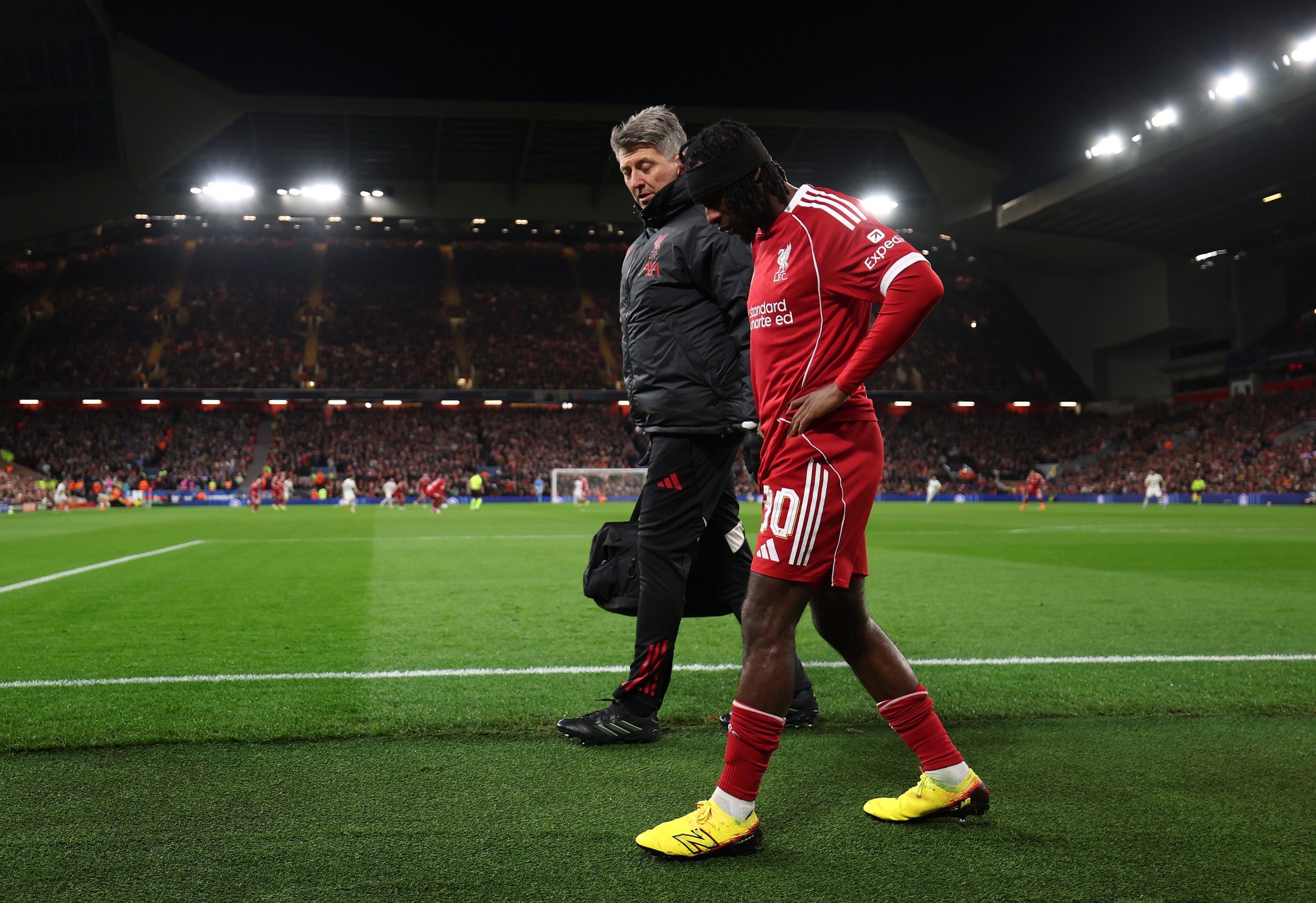 Jeremie Frimpong holds his side as he walks on the side of the pitch with a Liverpool physio.